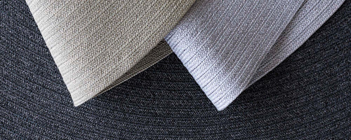 To strukturerede tæppeprøver i lyse farver, der viser kontrasterende mønstre mod en mørkere baggrund.