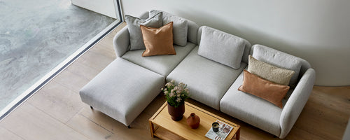 En stilfuld lys grå sofa med hyggelige puder, suppleret af et trækaffebord og en lille potteplante.