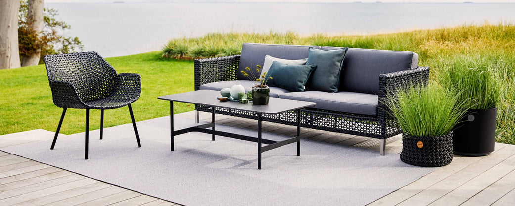 Stilfuld siddearrangement med en moderne sofa, lænestol og sofabord, suppleret med dekorative puder og grønt.
