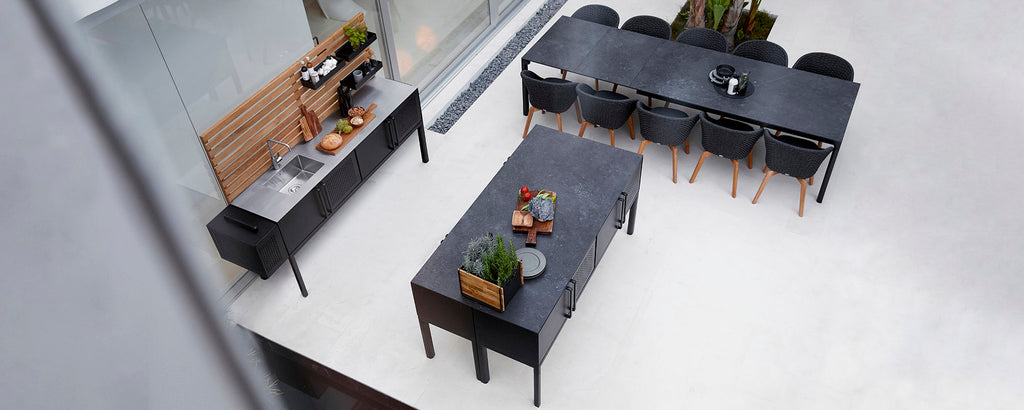 Aerial view of sleek dark tables and a sideboard, arranged with decorative plants and serving items.