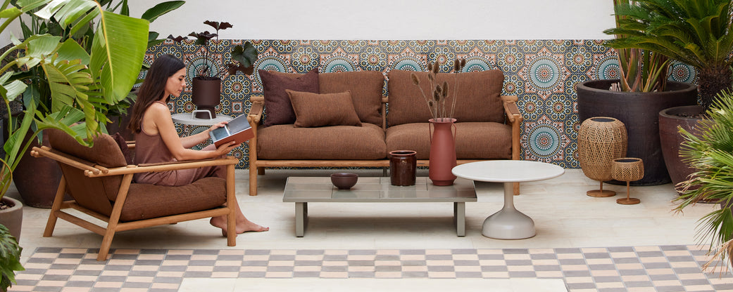 A cozy seating arrangement featuring a woman reading, surrounded by plants and decorative elements in earthy tones.