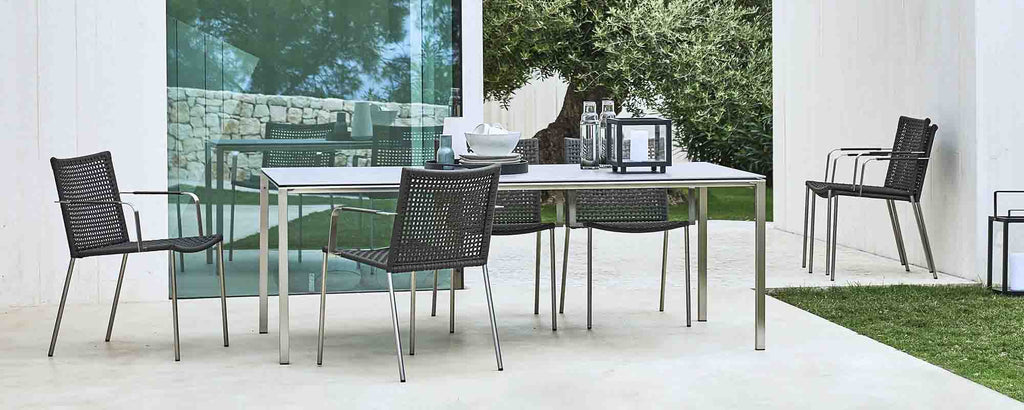 Modern dining setup featuring a sleek table with a pure finish and stylish straw chairs, surrounded by greenery. Perfect for gatherings.