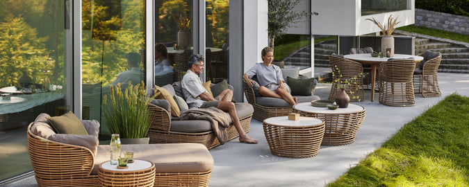 Moderne rattanstole med grå puder og et sofabord i en moderne udendørs loungeindstilling.
