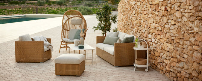 Moderne udendørs loungeområde med brun rattan-sofa og stole med beige puder.