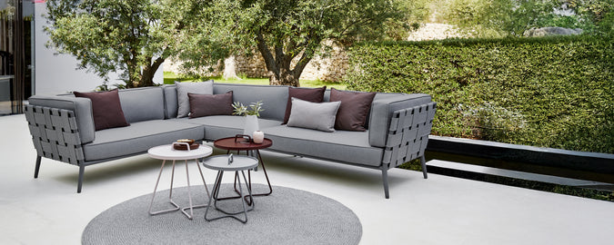 Moderne grå sektion sofa med lilla puder og et rundt sofabord i et loungeområde.