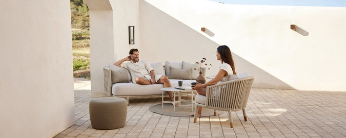 Moderne loungeområde med beige sofa, hvide puder, grå stol og rundt bord.