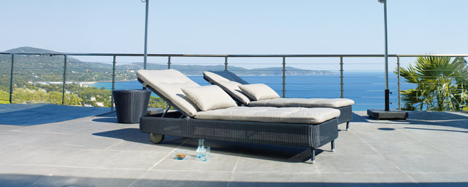 To moderne grå og sorte loungestole på en terrasse med udsigt over havet.