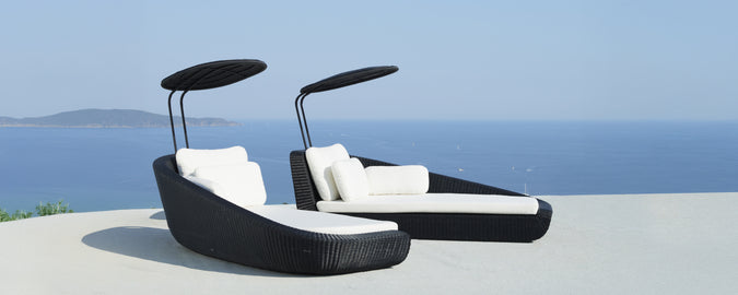 Moderne sorte loungestole med hvide puder med udsigt over havet.