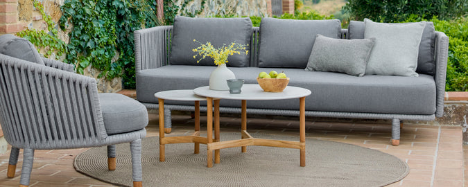 Moderne udendørs loungeområde med en grå sofa, grå stol og et trækaffebord.