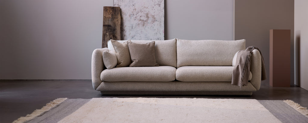 Beige sofa med grå puder i et moderne lounge-miljø.