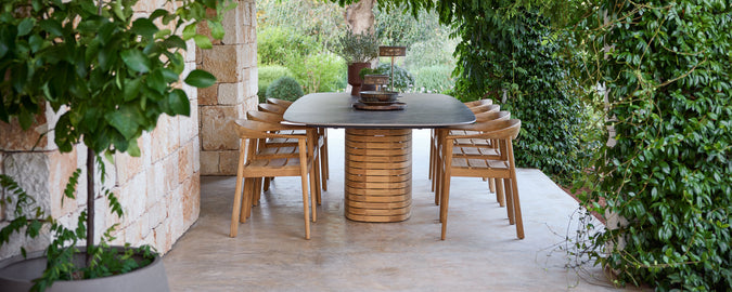 Udendørs træspisestole omkring et sorte bord i en grøn have.