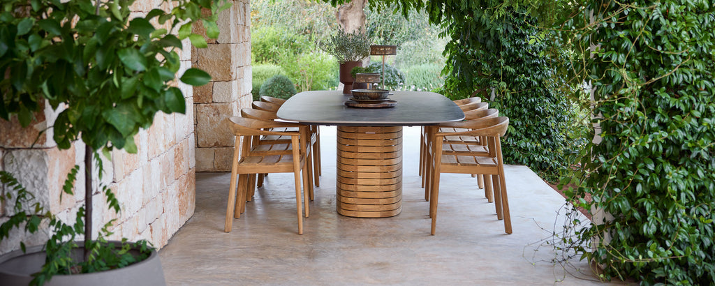 Udendørs træspisestole omkring et sorte bord i en grøn have.