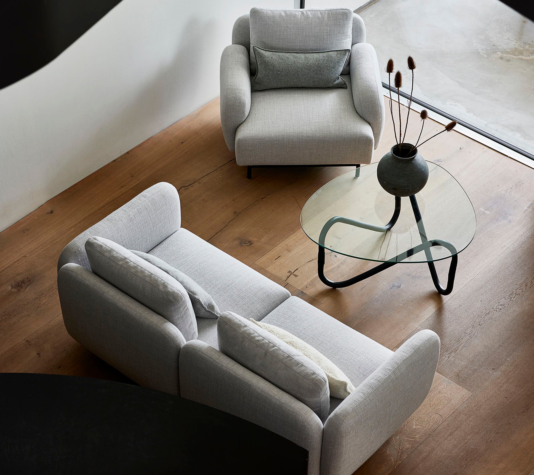 Stilfulde grå sofaer og et elegant glas sofabord med dekorative elementer på bordpladen, sat mod et varmt trægulv.