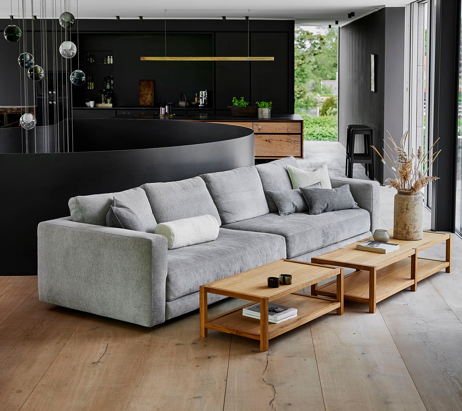 En moderne, grå sofa med bløde puder ved siden af trækaffeborde i en nutidig indstilling med stilfuld indretning.