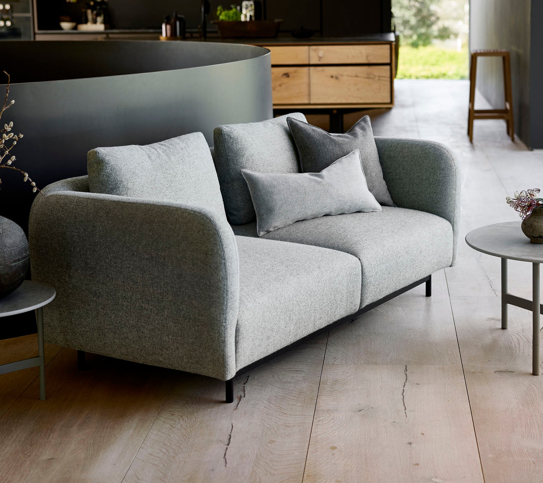 Moderne grå sofa med bløde puder, parret med et lille rundt bord, sat mod en minimalistisk baggrund.