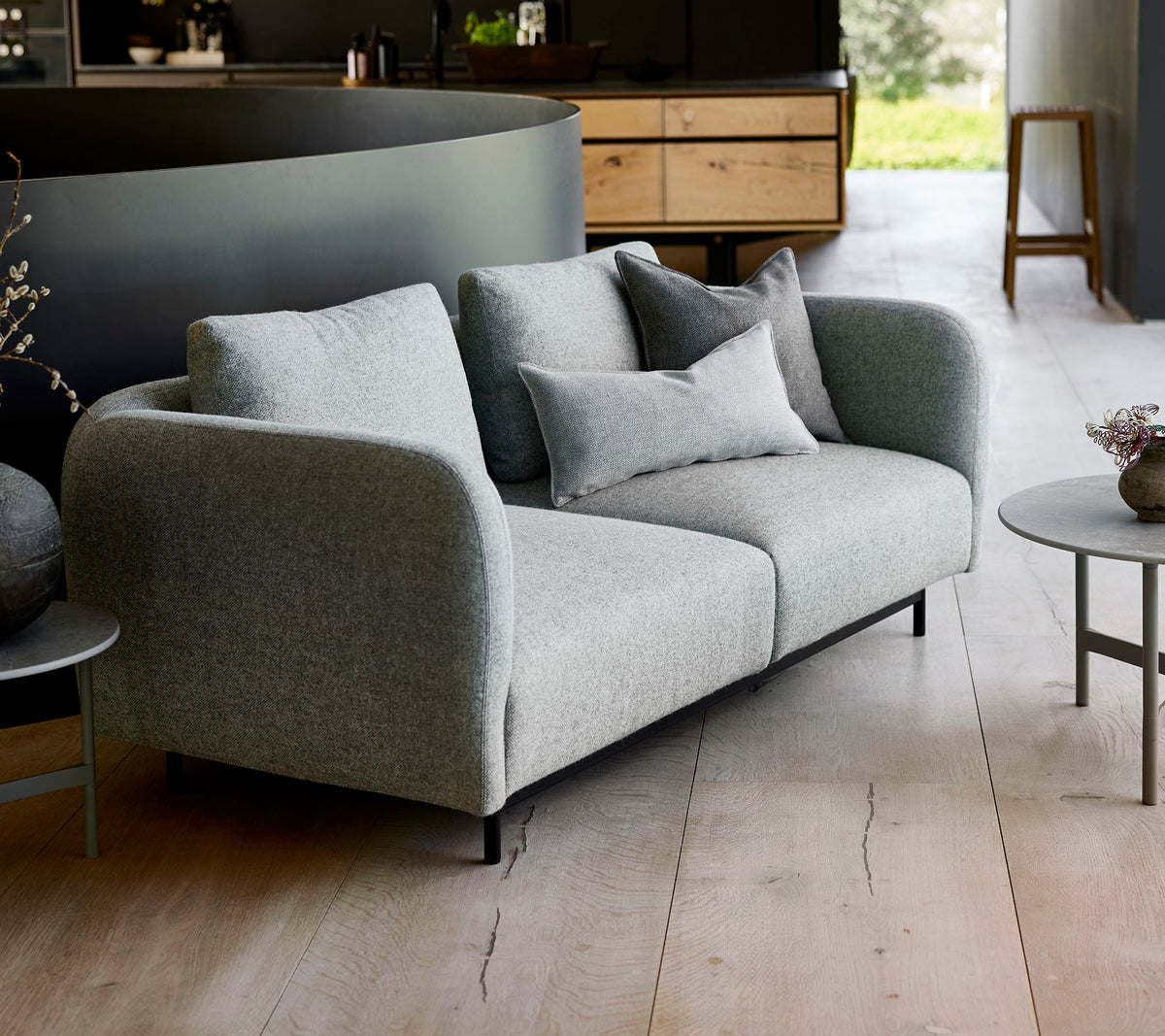 Moderne grå sofa med bløde puder, parret med et lille rundt bord, sat mod en minimalistisk baggrund.