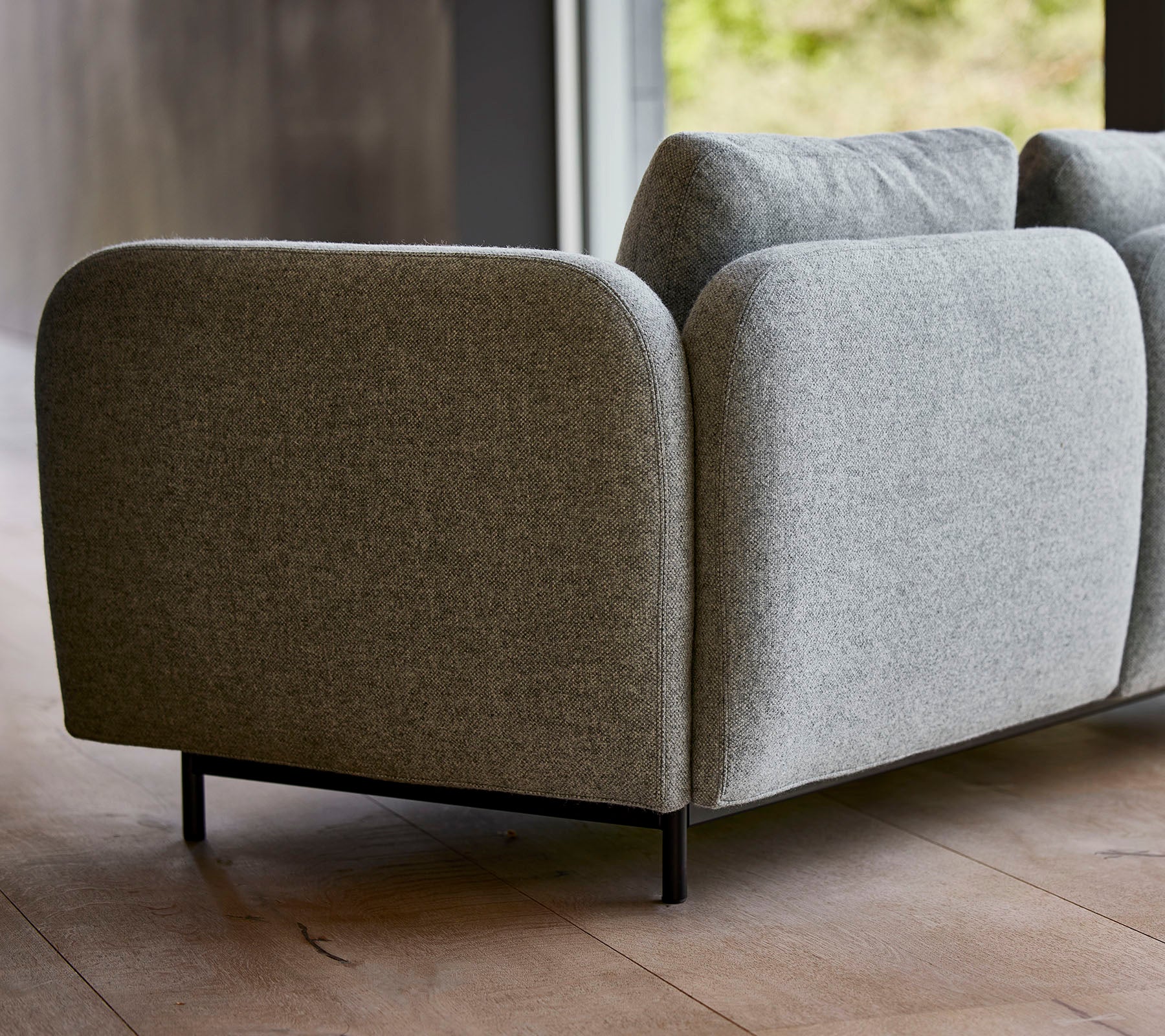En moderne grå polstret sofa med rundede kanter og slanke sorte ben, der viser et minimalistisk design.