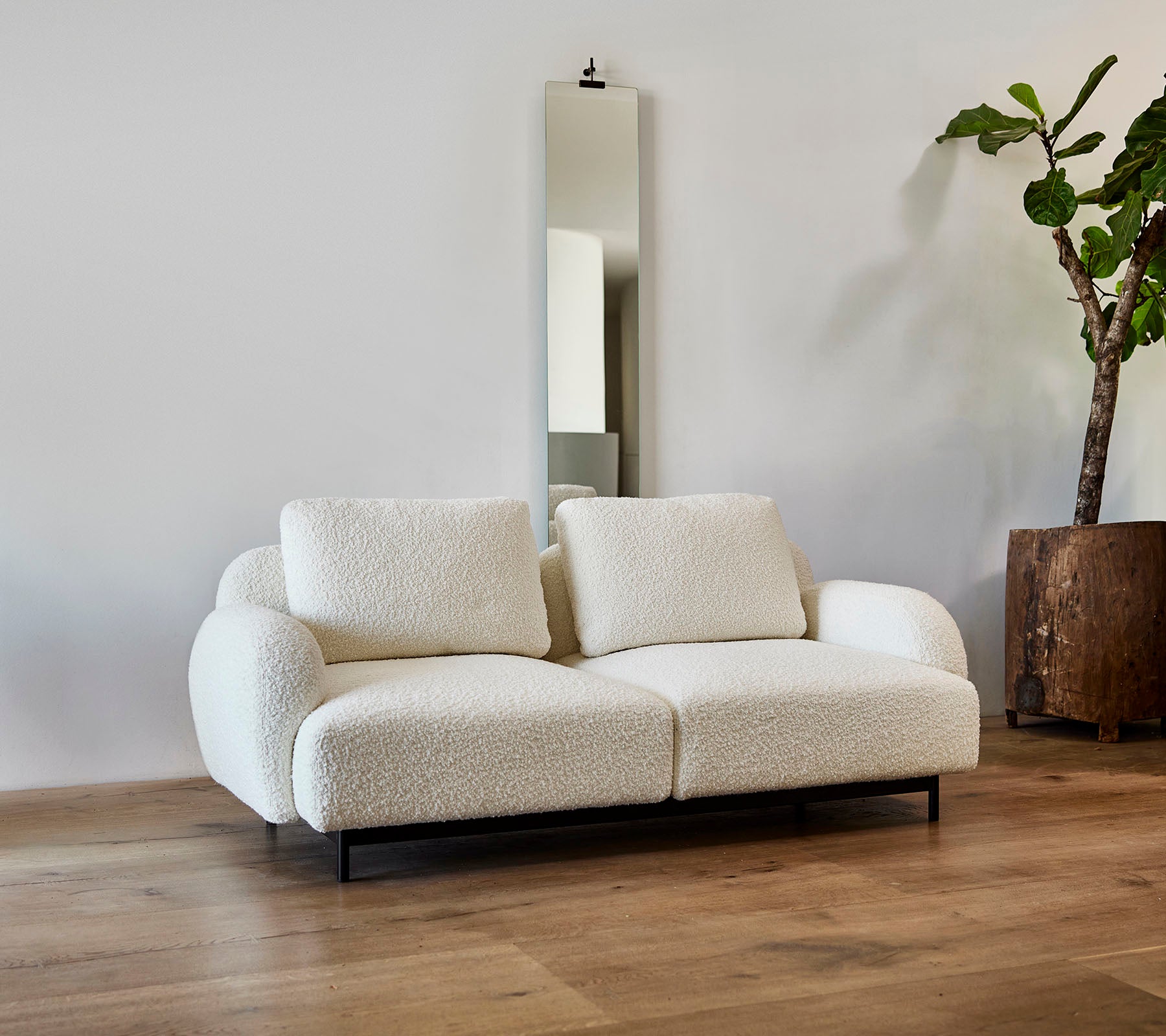 En stilfuld hvid sofa med bløde puder, kombineret med et stort spejl og en potteplante i en moderne indretning.