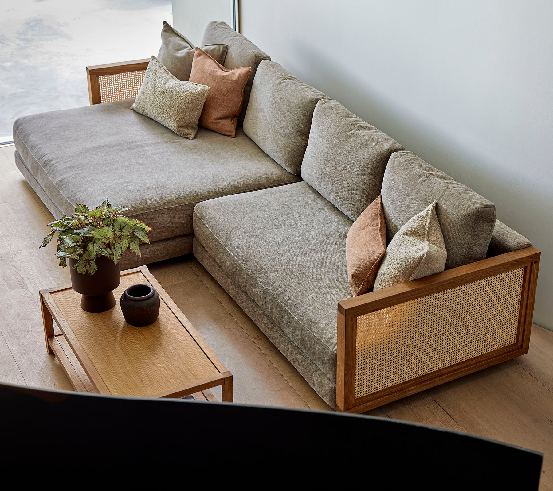 En stilfuld sectional sofa med bløde puder og dekorative puder, parret med et trækaffebord med planter og elegant dekoration.