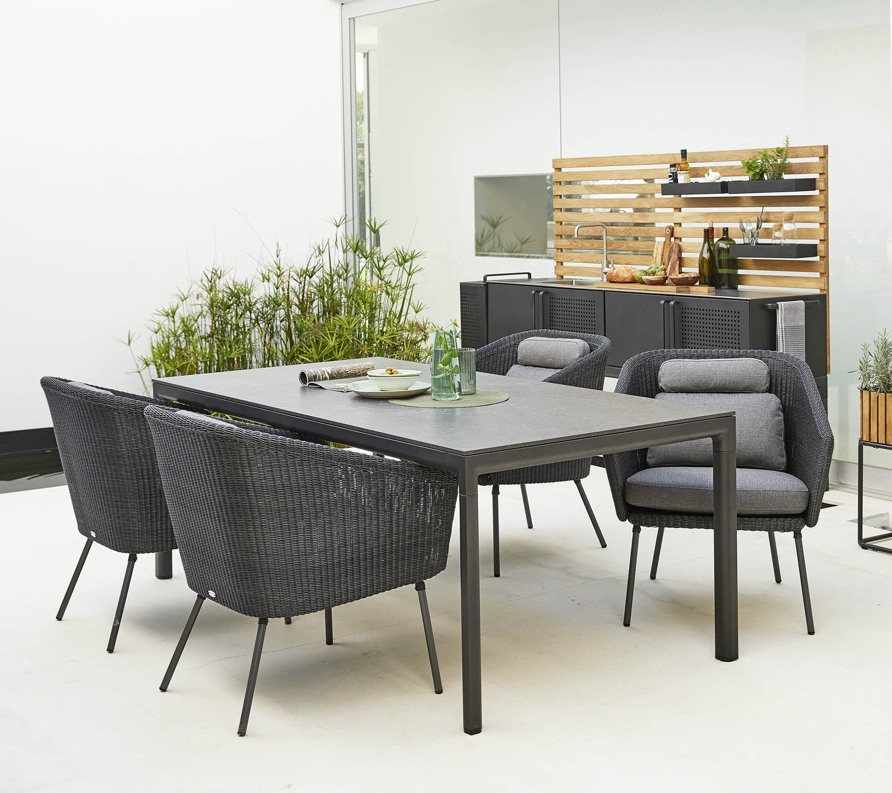 Stilfuld udendørs spisestue sæt med et slankt bord og komfortable, moderne stole omgivet af dekorativt grønt.