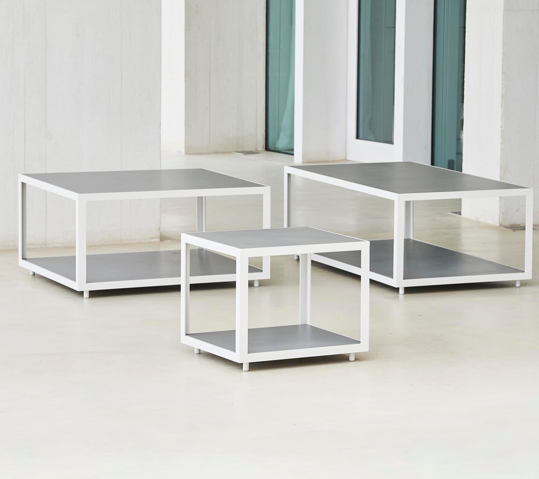 Et sæt af tre moderne borde med et slankt design, der har metalrammer og flade overflader, arrangeret i forskellige størrelser.