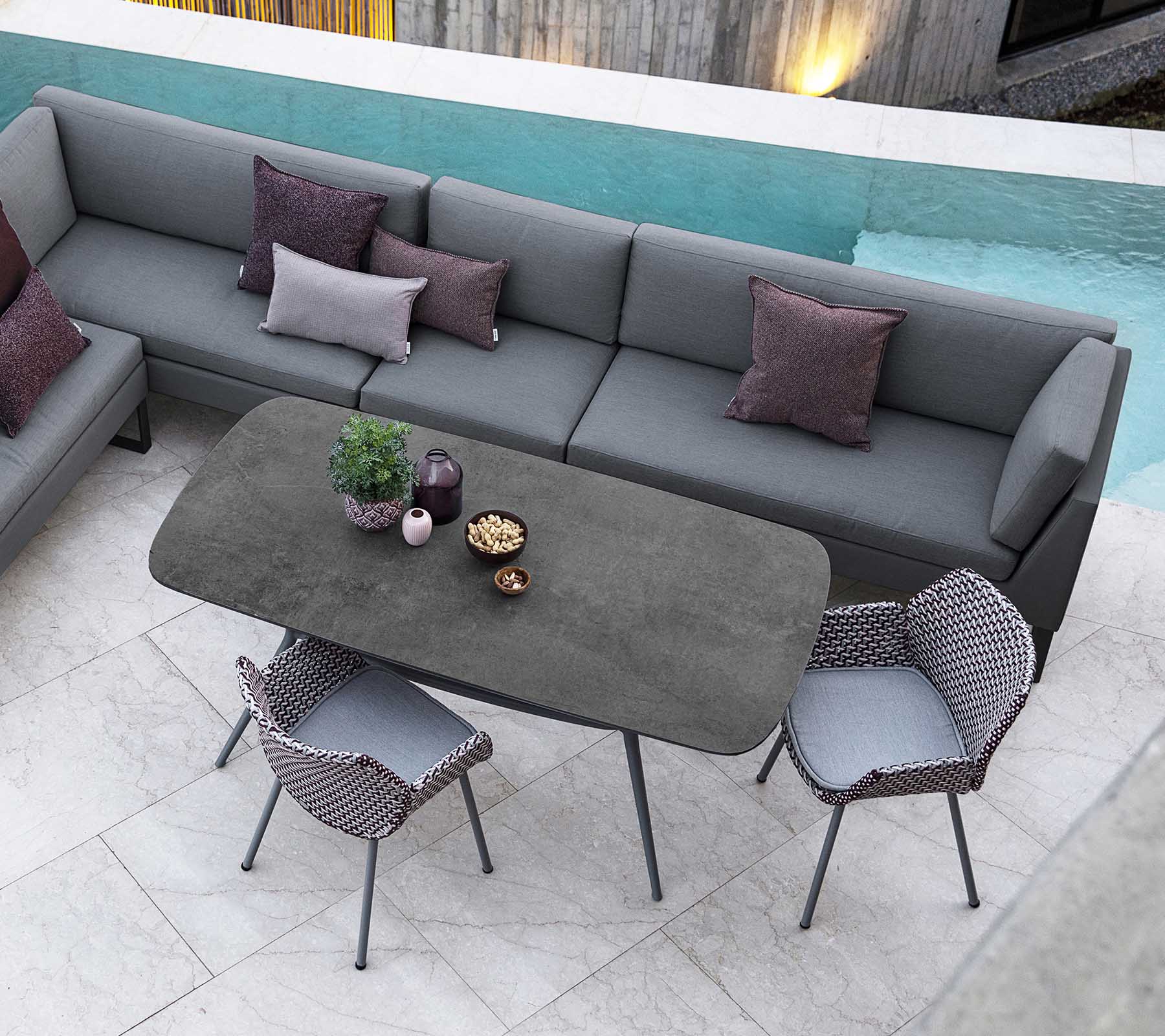 Moderne udendørs siddeområde med en modulsofa med puder, et elegant rektangulært bord og stilfulde stole, suppleret af udsigt til poolen.