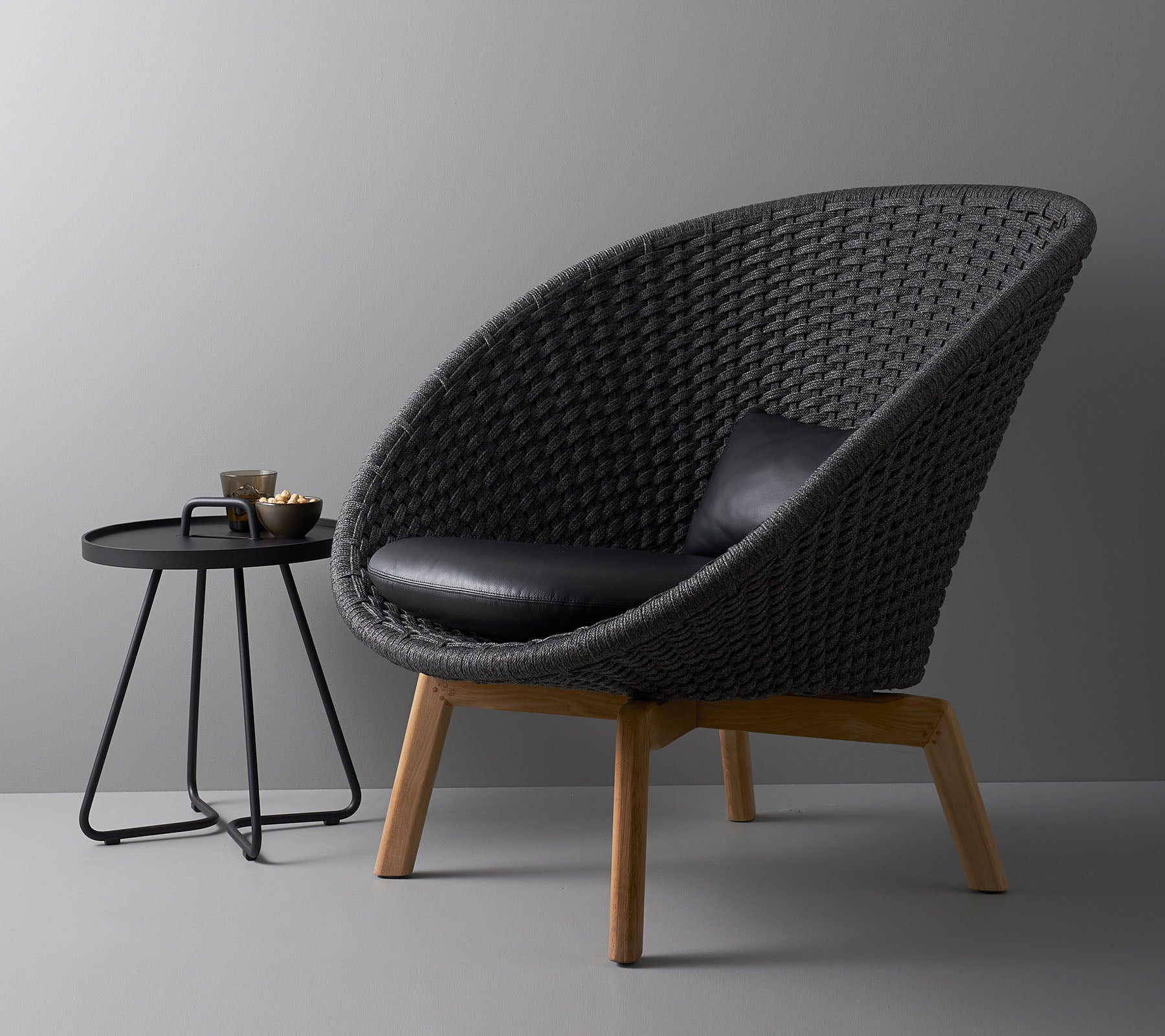 Stilfuld vævet stol med en sort pude og et moderne rundt sidebord, ideelt til nutidige boligområder.