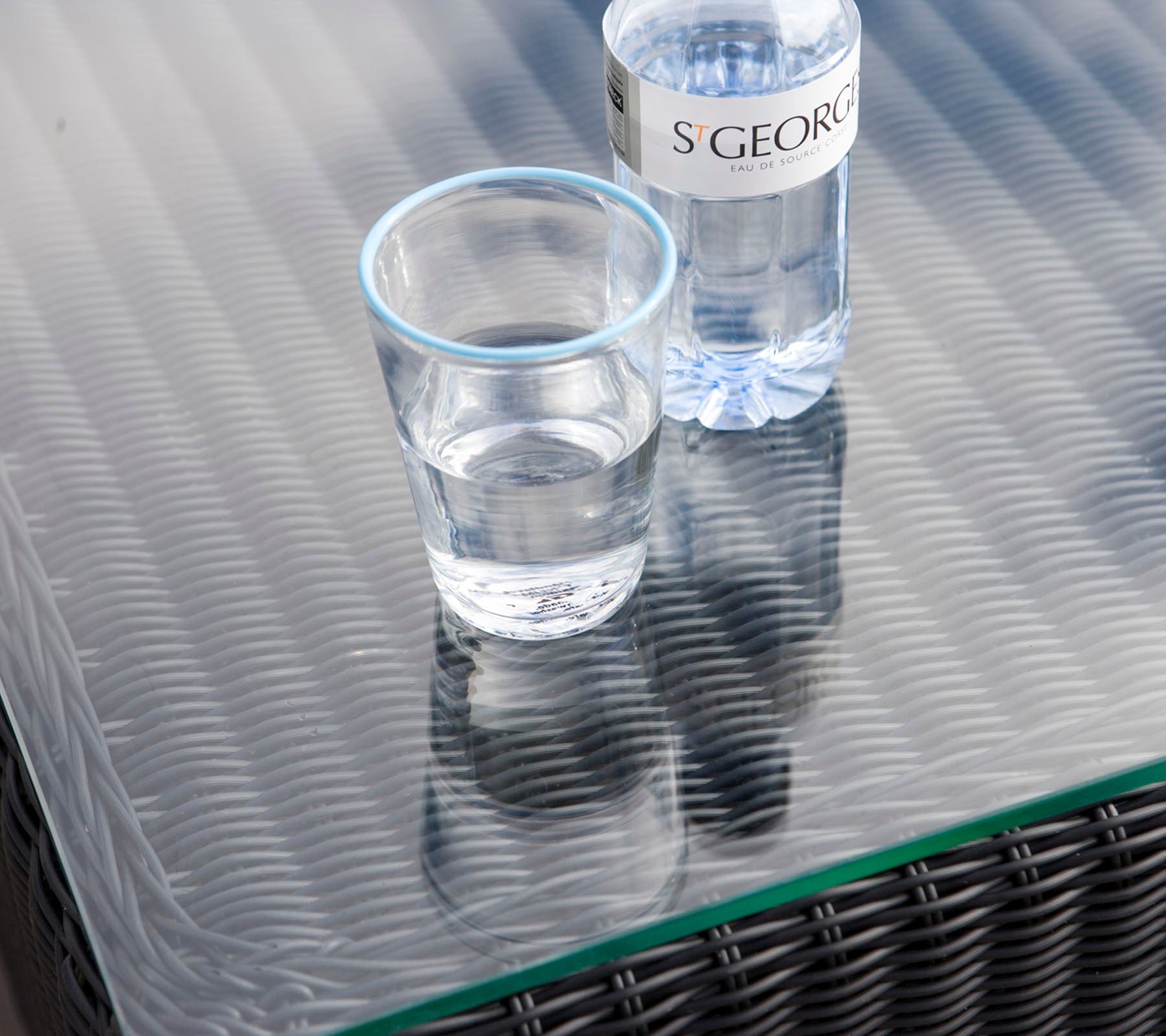 Et klart glas med vand ved siden af en vandflaske på en tekstureret bordflade.