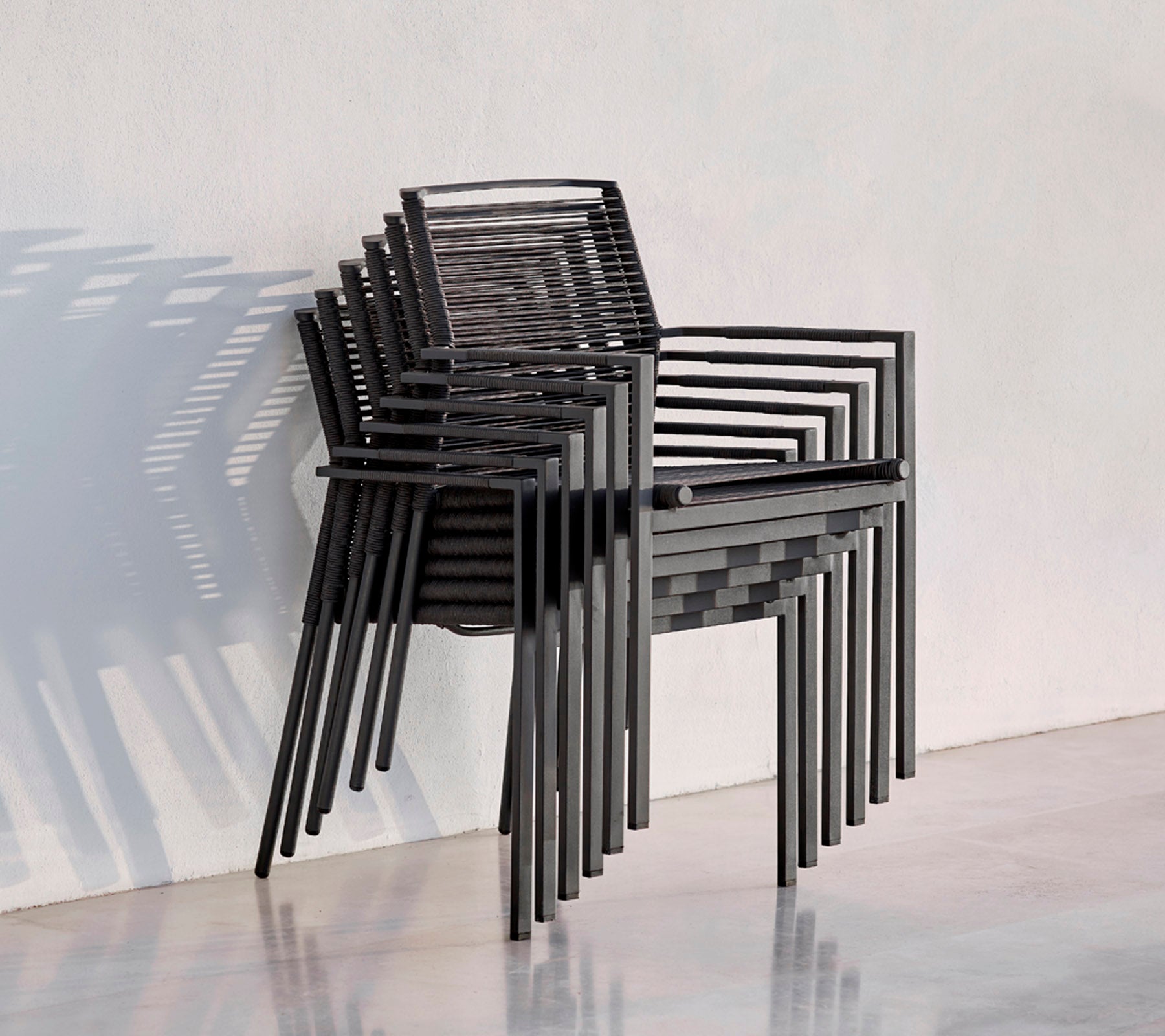 Et stak moderne sorte stole med et strømlinet design, der kaster skygger mod en lys baggrund.