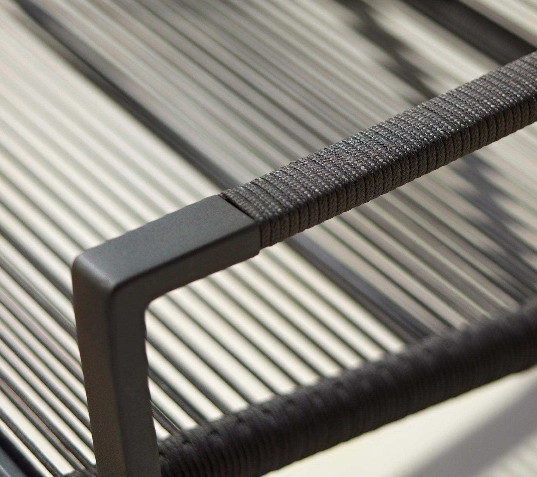 Nærbillede af en moderne stolers armlæn med et strømlinet design, teksturerede detaljer og en minimalistisk sort finish.