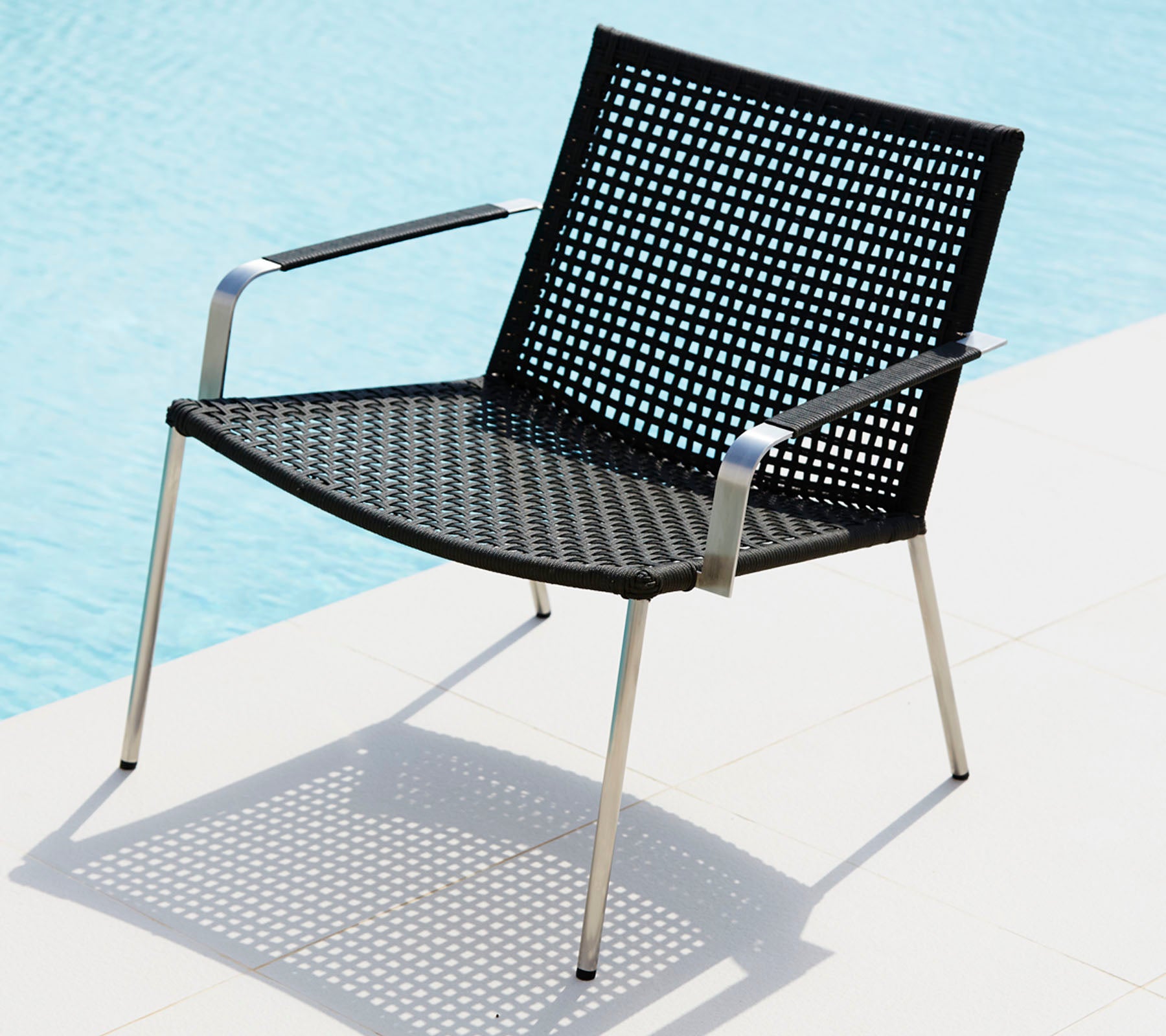 Stilfuld sort stol med et perforeret design og slanke metalben, der kaster skygge på en lys overflade.