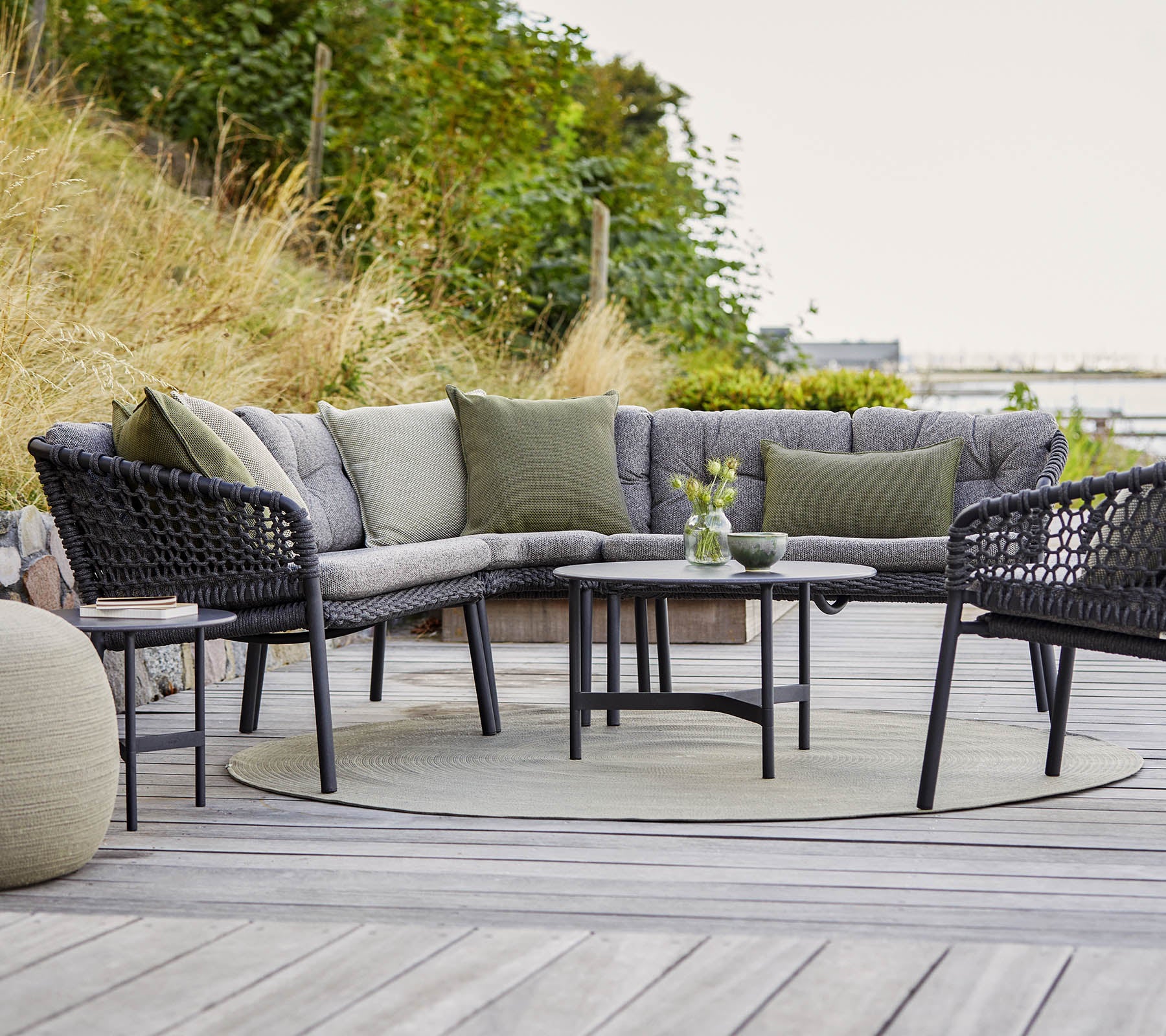 Stilfuld udendørs siddearrangement med et buet sectionalsofa, rundt bord og hyggelige accenter i en naturlig ramme.