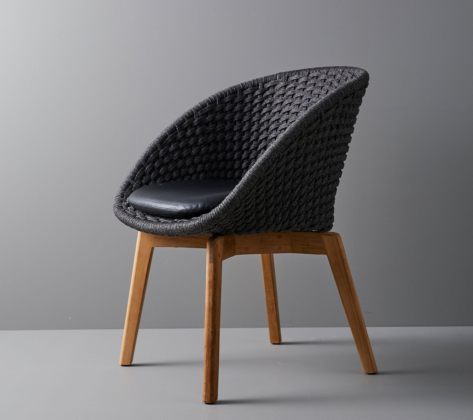 Stilfuld vævet stol med en komfortabel pude, der har glatte, tapede træben og et moderne design velegnet til forskellige omgivelser.