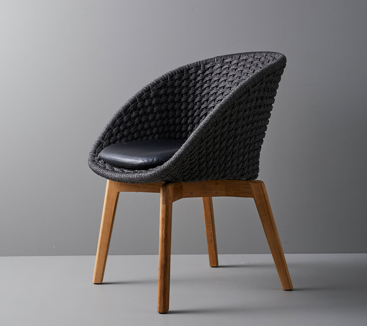 Stilfuld vævet stol med en komfortabel pude, der har glatte, tapede træben og et moderne design velegnet til forskellige omgivelser.
