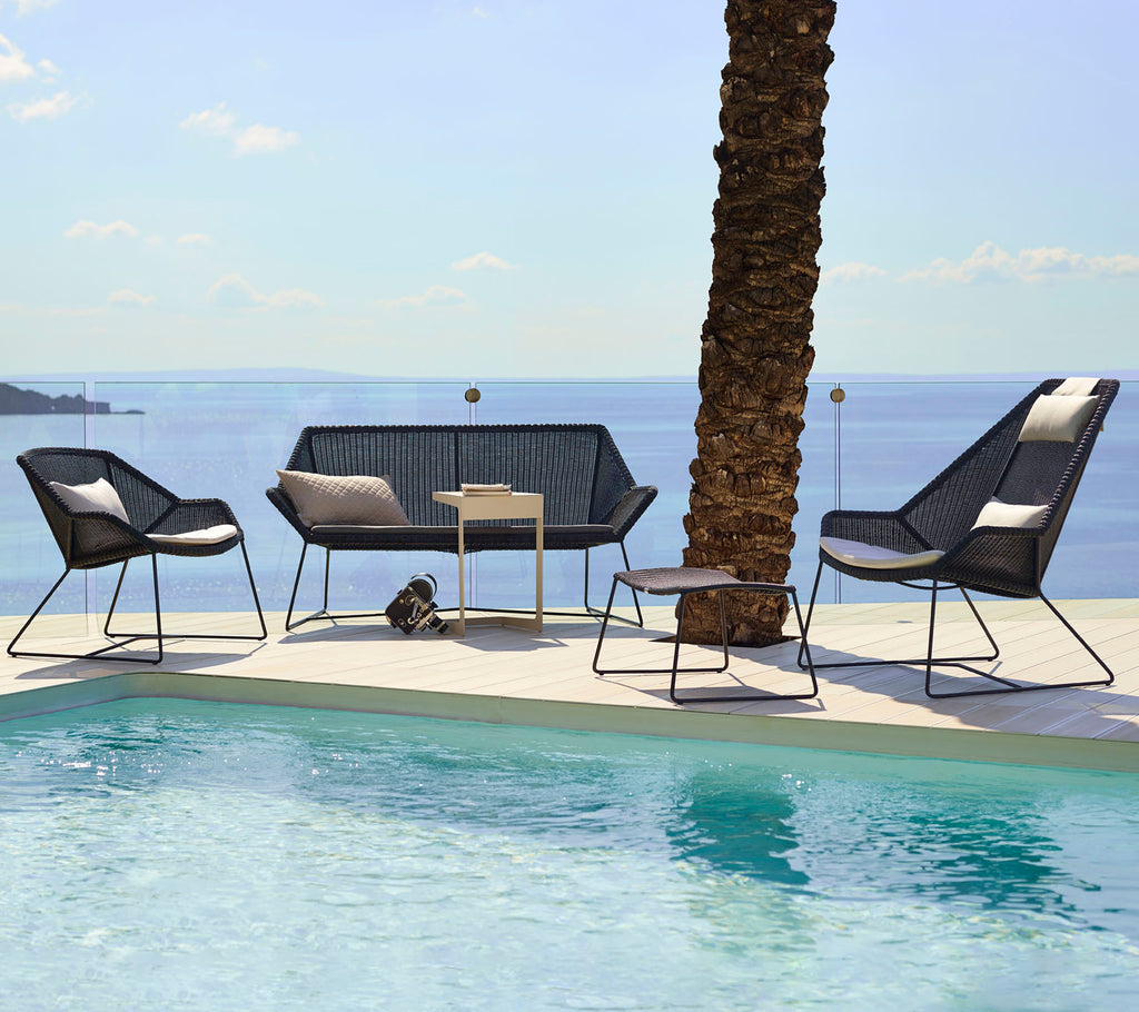 Moderne loungesæder med sorte stole og en loveseat ved siden af en pool.