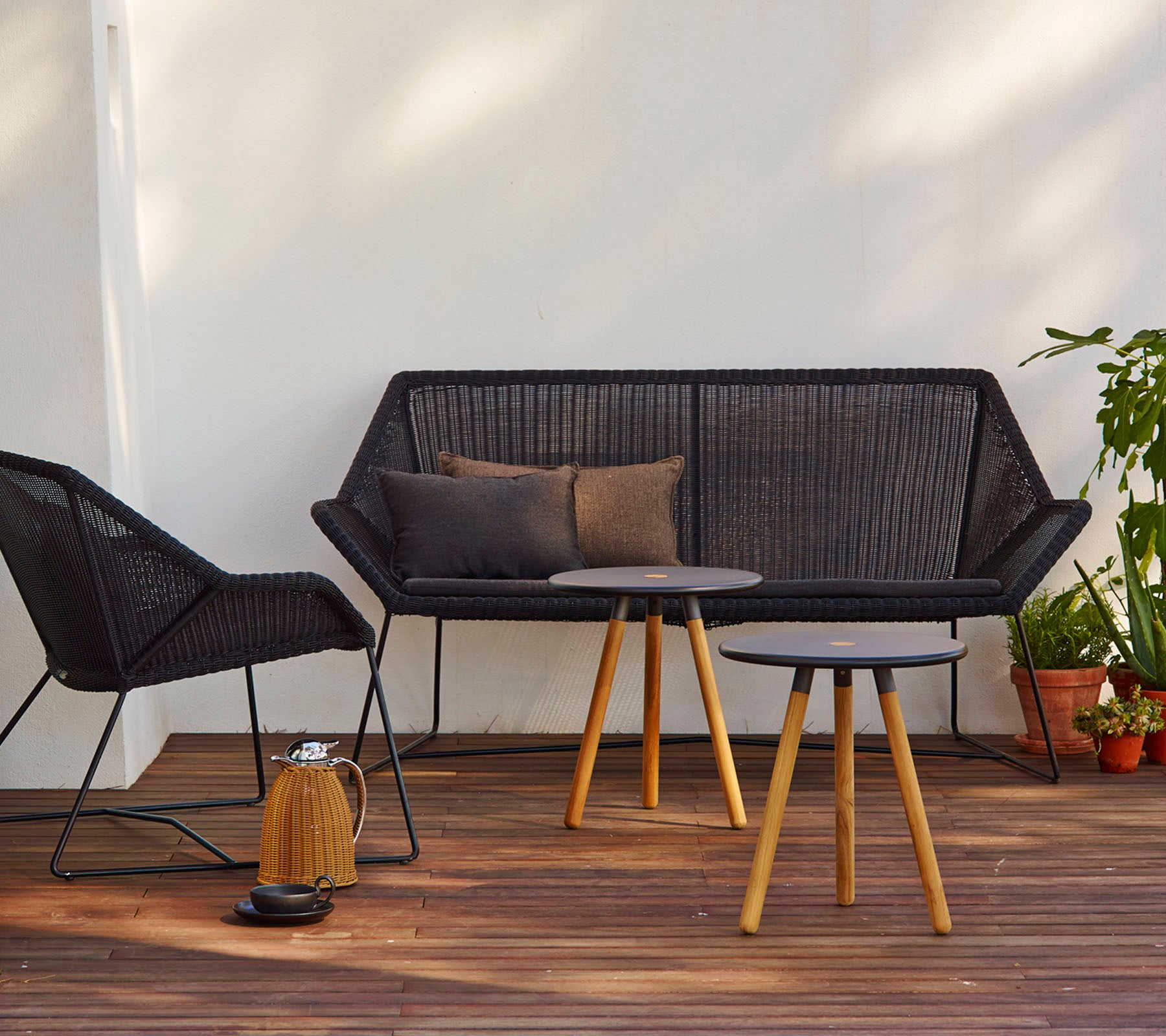 Moderne siddearrangement med en sort sofa med puder, en matchende stol og et rundt bord med træben.