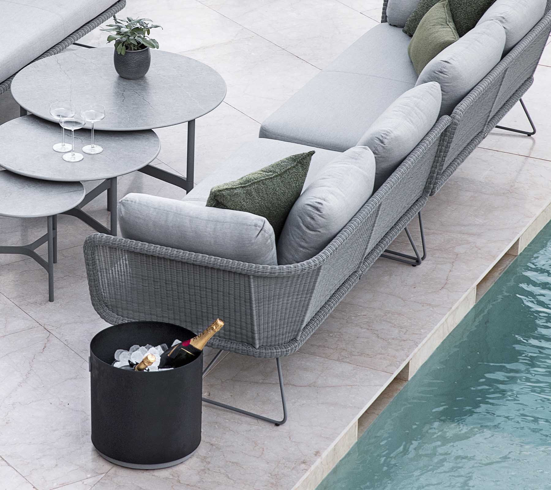 Moderne udendørs siddearrangement med en stilfuld grå sofa og et rundt bord, suppleret med en spand is og drinks.