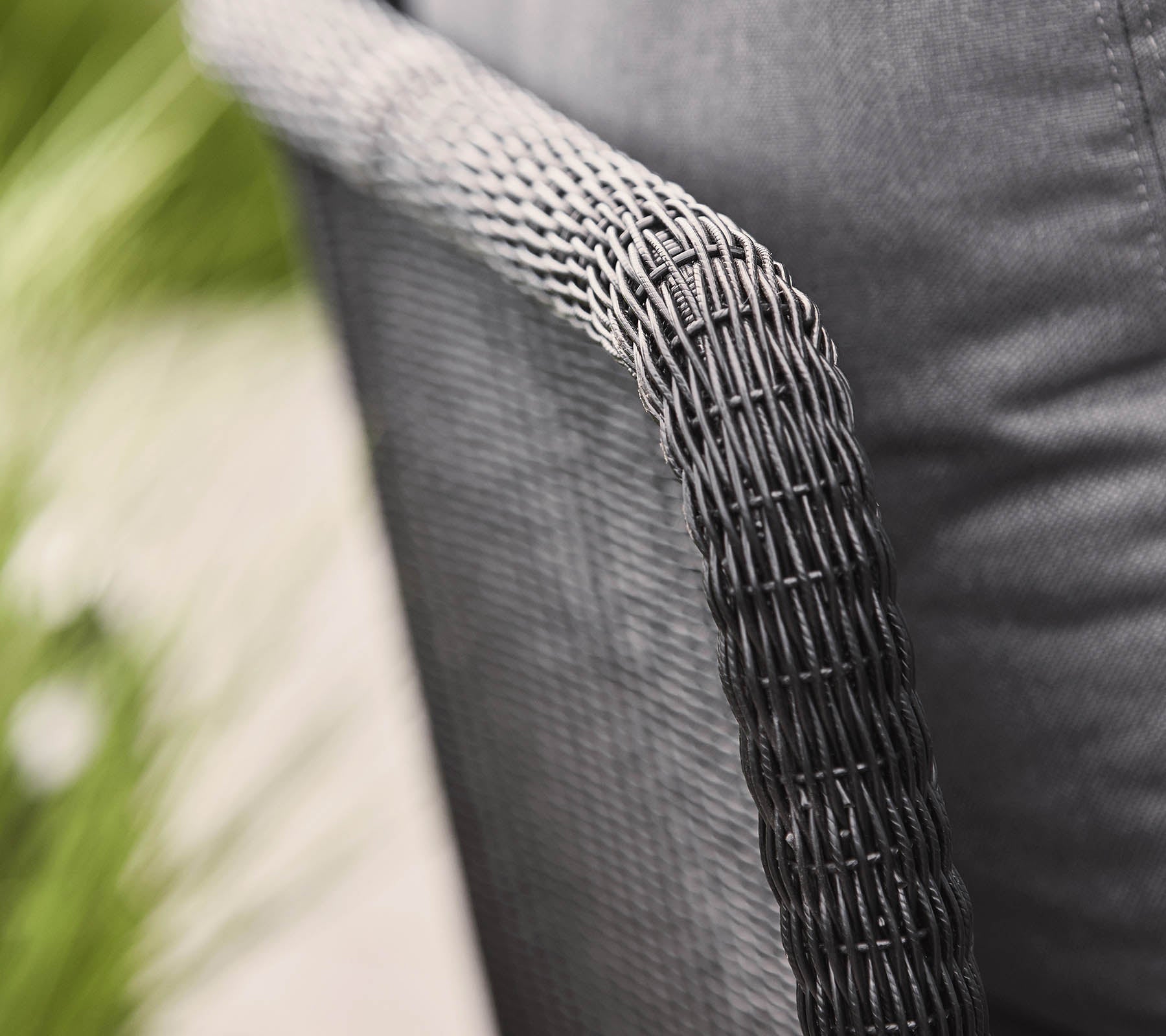 Nærbillede af et vævet stolarm med en struktureret sort finish, der viser et moderne design og en hyggelig stofsæde.