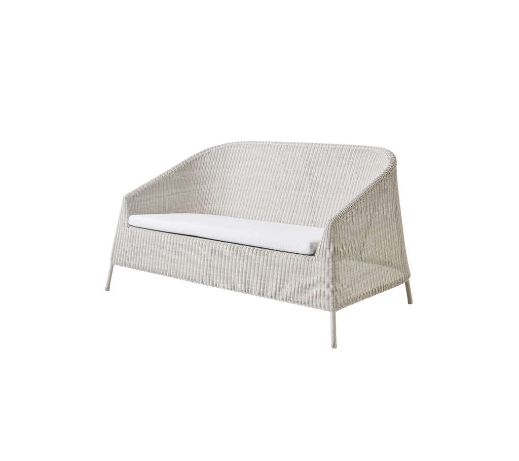 Moderne sandfarvet kærestesofa med en hvid pude i et minimalistisk design.