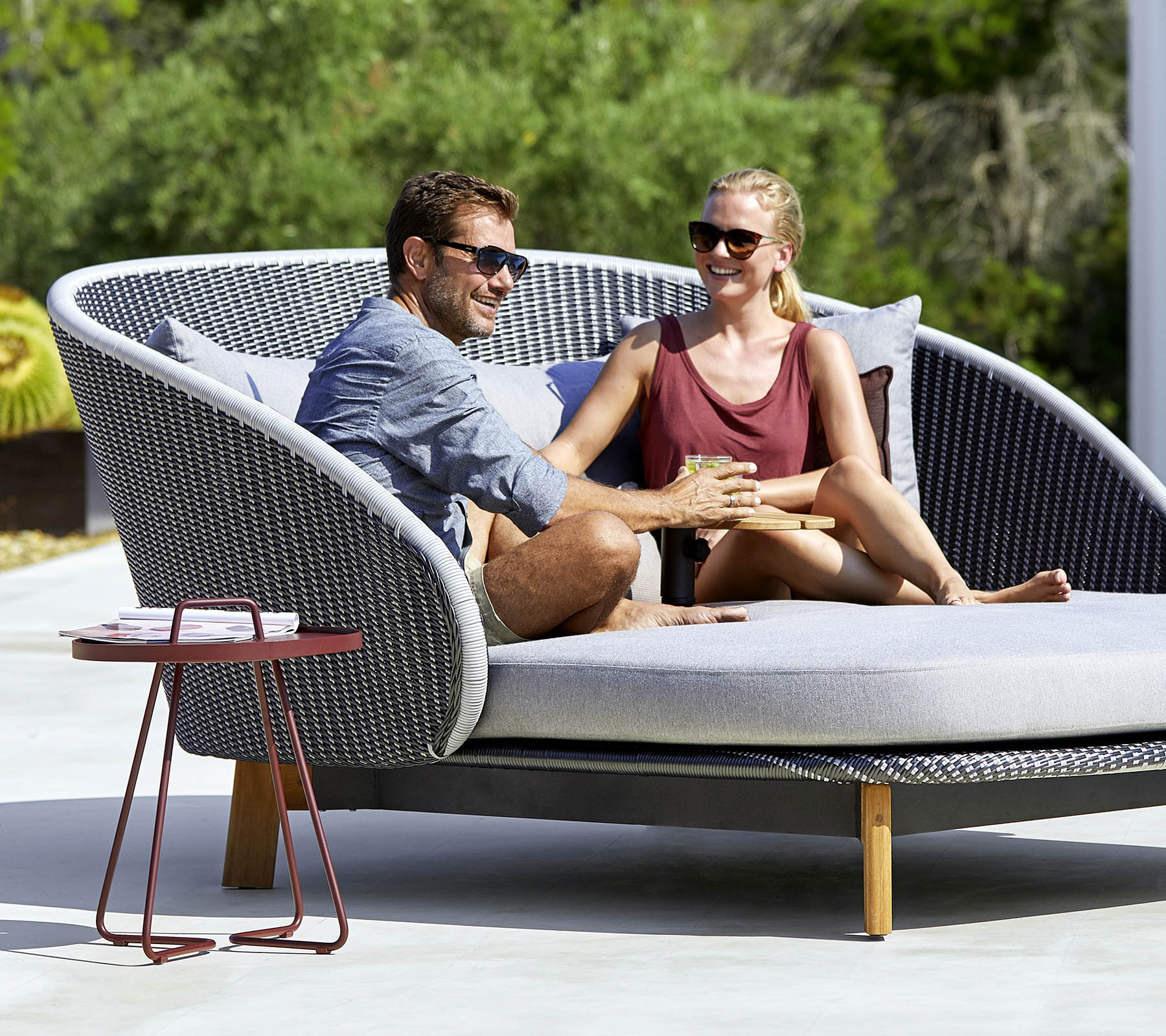 Et par nyder et hyggeligt øjeblik sammen på en stilfuld, buet udendørs sofa med et sidebord i nærheden.