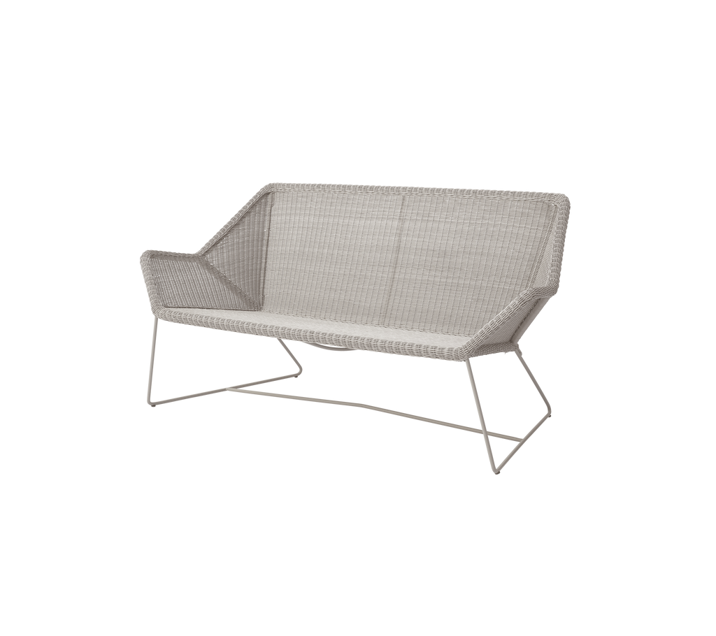Moderne sandfarvet sofa med et slankt design i en loungeindstilling.