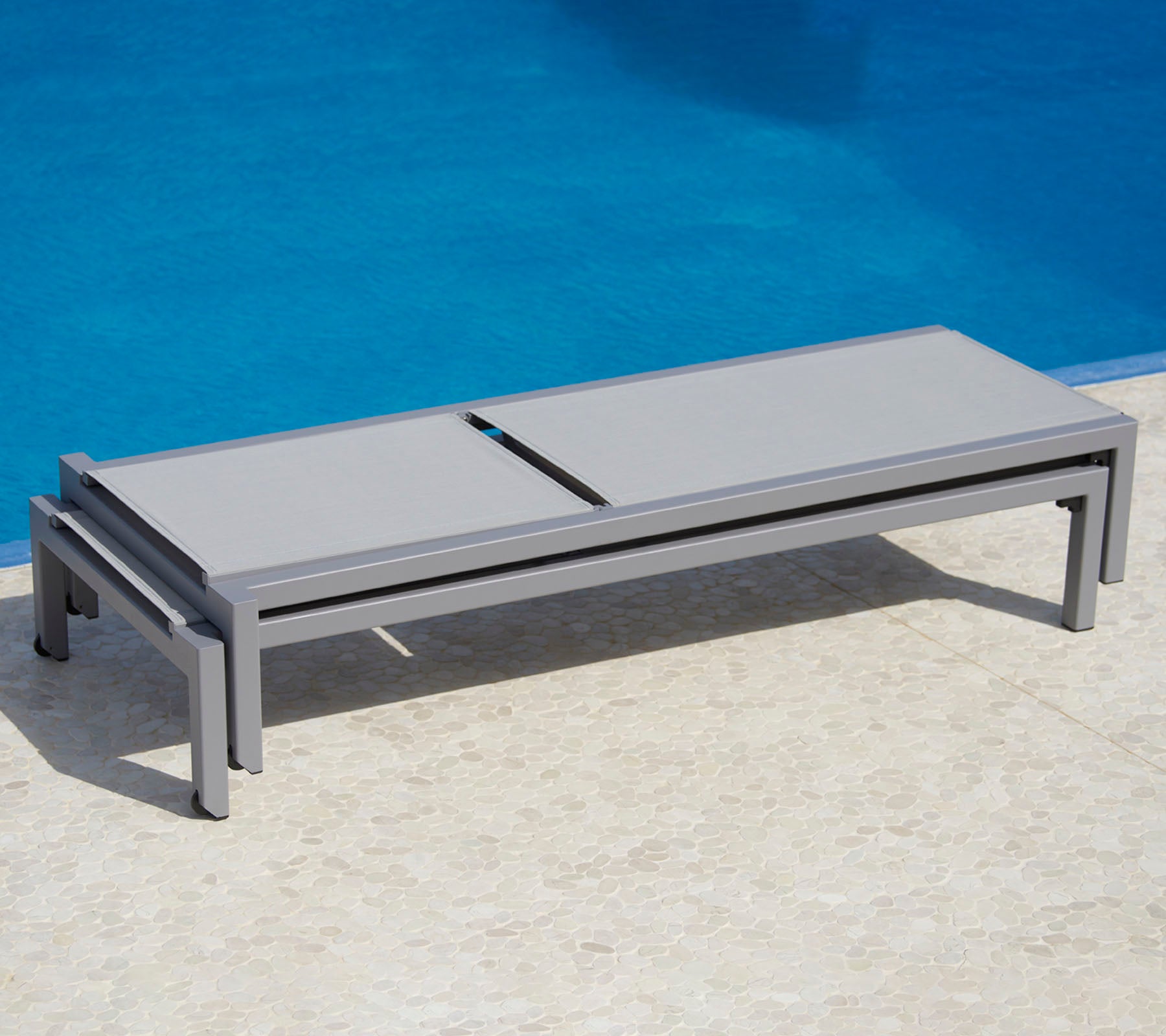Stilfuld grå loungeseng ved en pool, der har et slankt design og praktisk funktionalitet til afslapning.