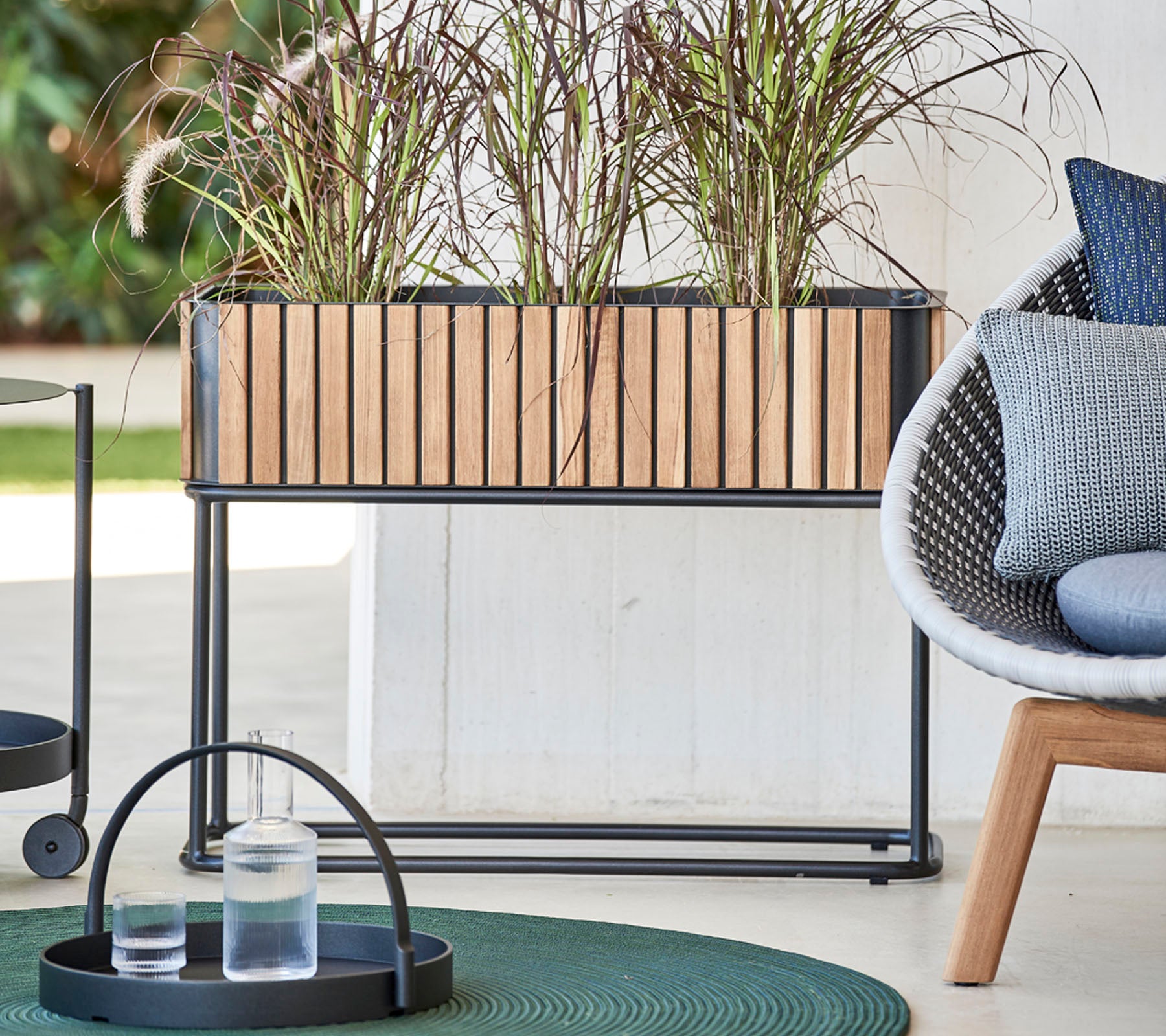 Træ plantekasse med dekorative planter, ledsaget af en rund bakke med glas og en moderne stol med bløde puder.