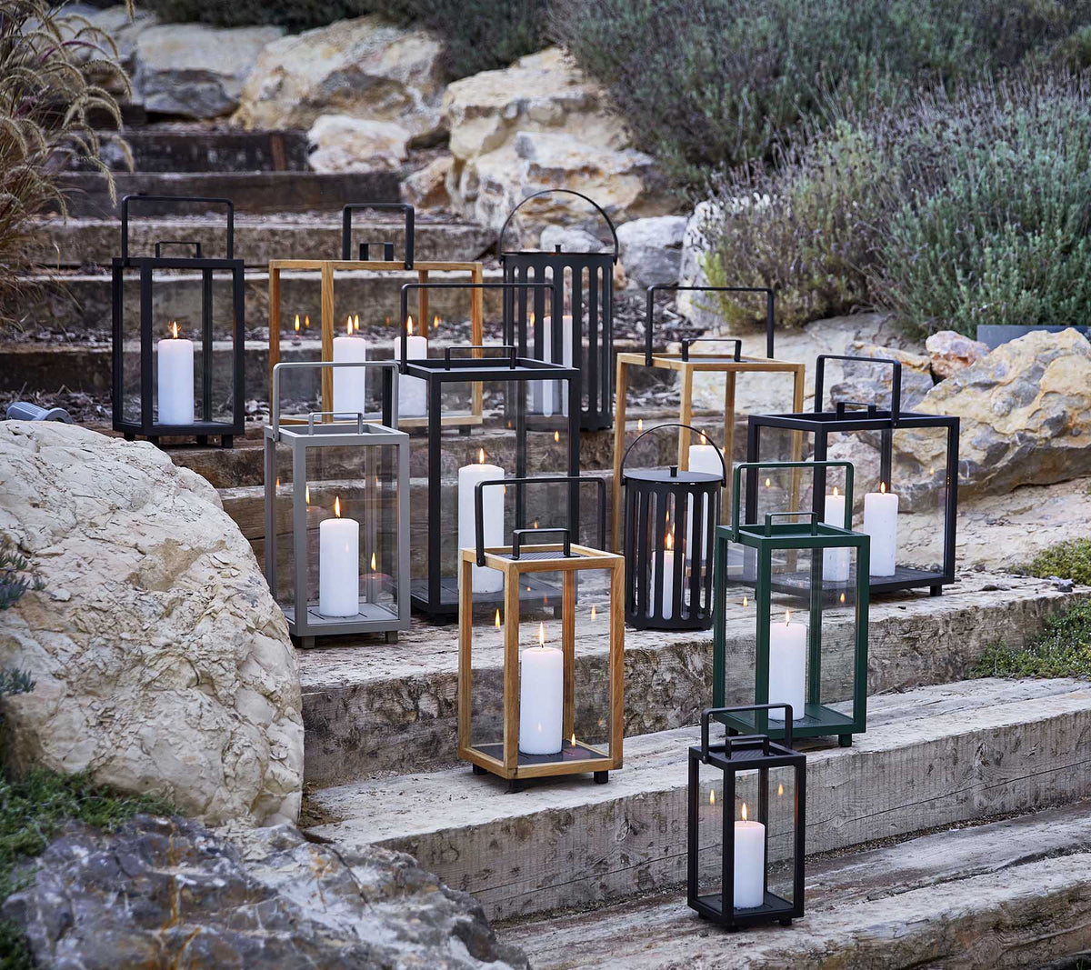 Samling af dekorative lanterner i forskellige stilarter og farver, med blødt stearinlyslys, kunstnerisk arrangeret på stentrin.