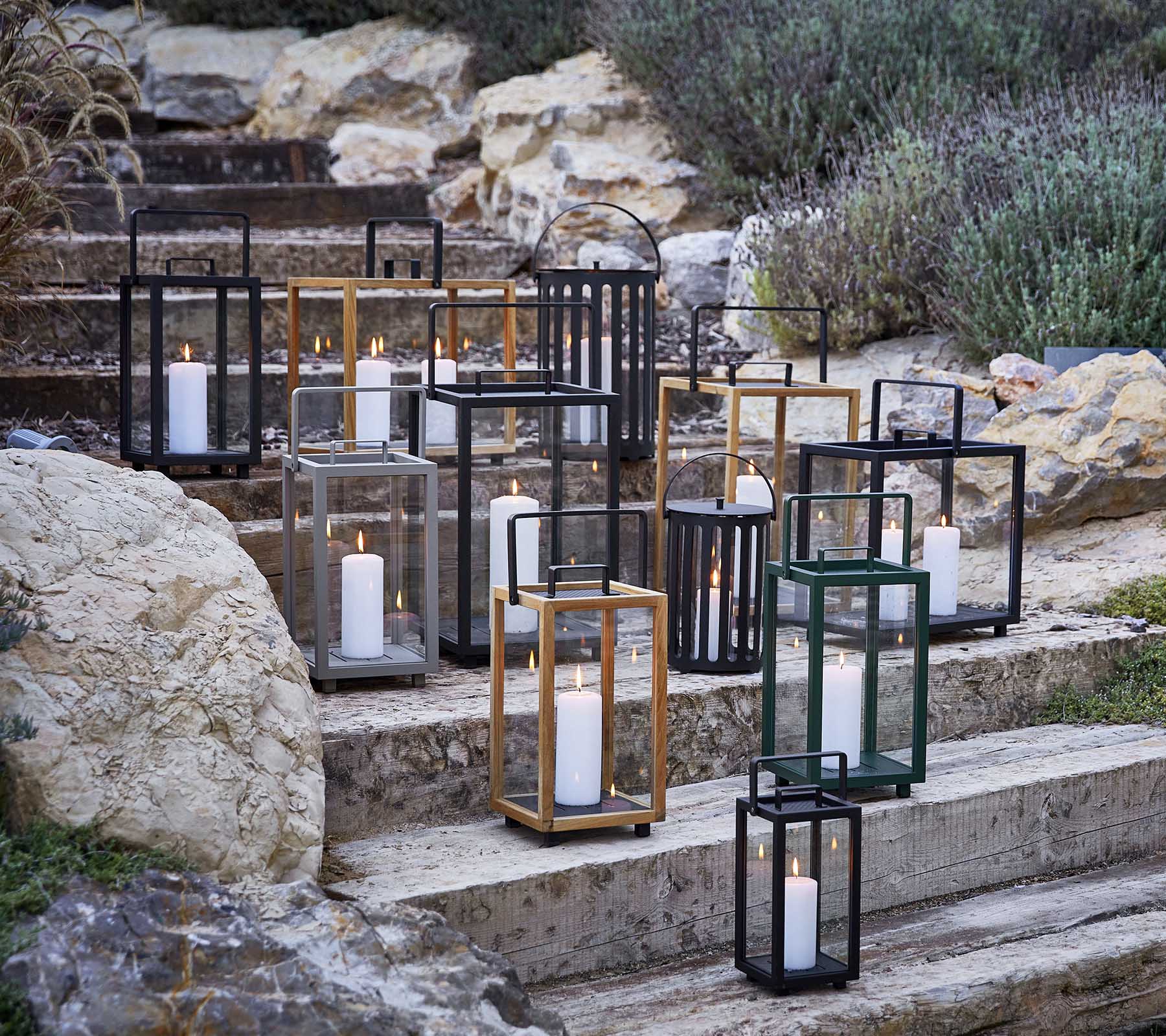 Samling af dekorative lanterner i forskellige stilarter og farver, med blødt stearinlyslys, kunstnerisk arrangeret på stentrin.
