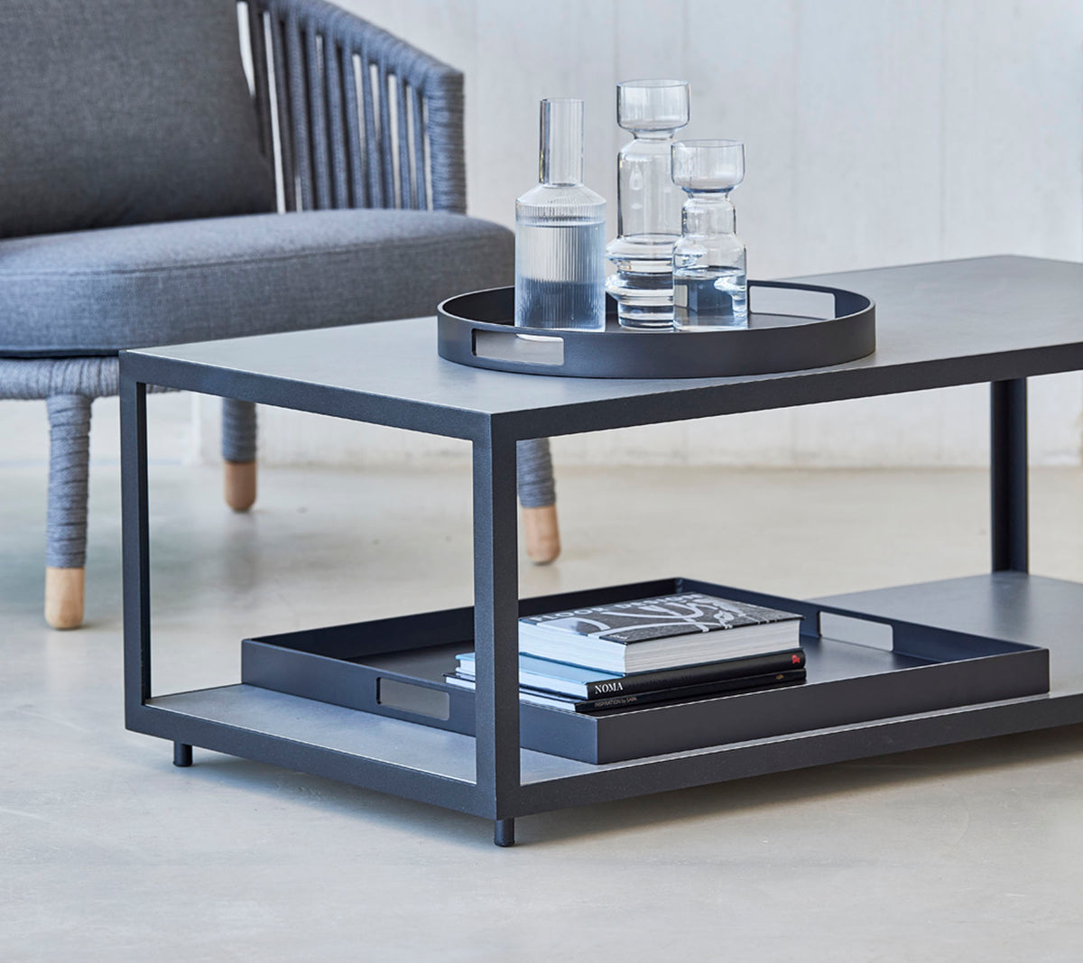 Moderne sofabord med et slankt design, med en bakke, glas og bøger på den nederste hylde. Ideelt til stilfulde opholdsområder.