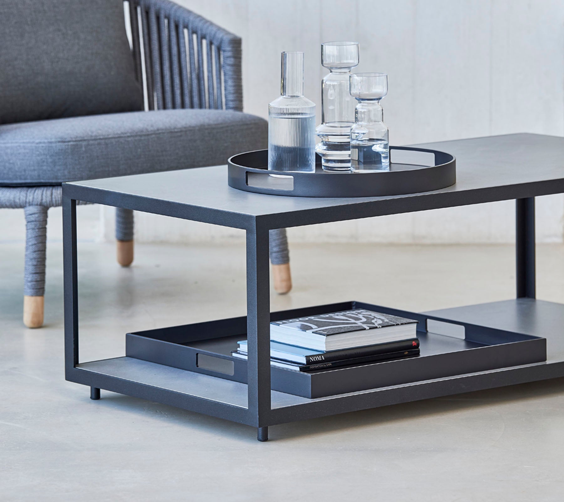 Moderne sofabord med et slankt design, med en bakke, glas og bøger på den nederste hylde. Ideelt til stilfulde opholdsområder.