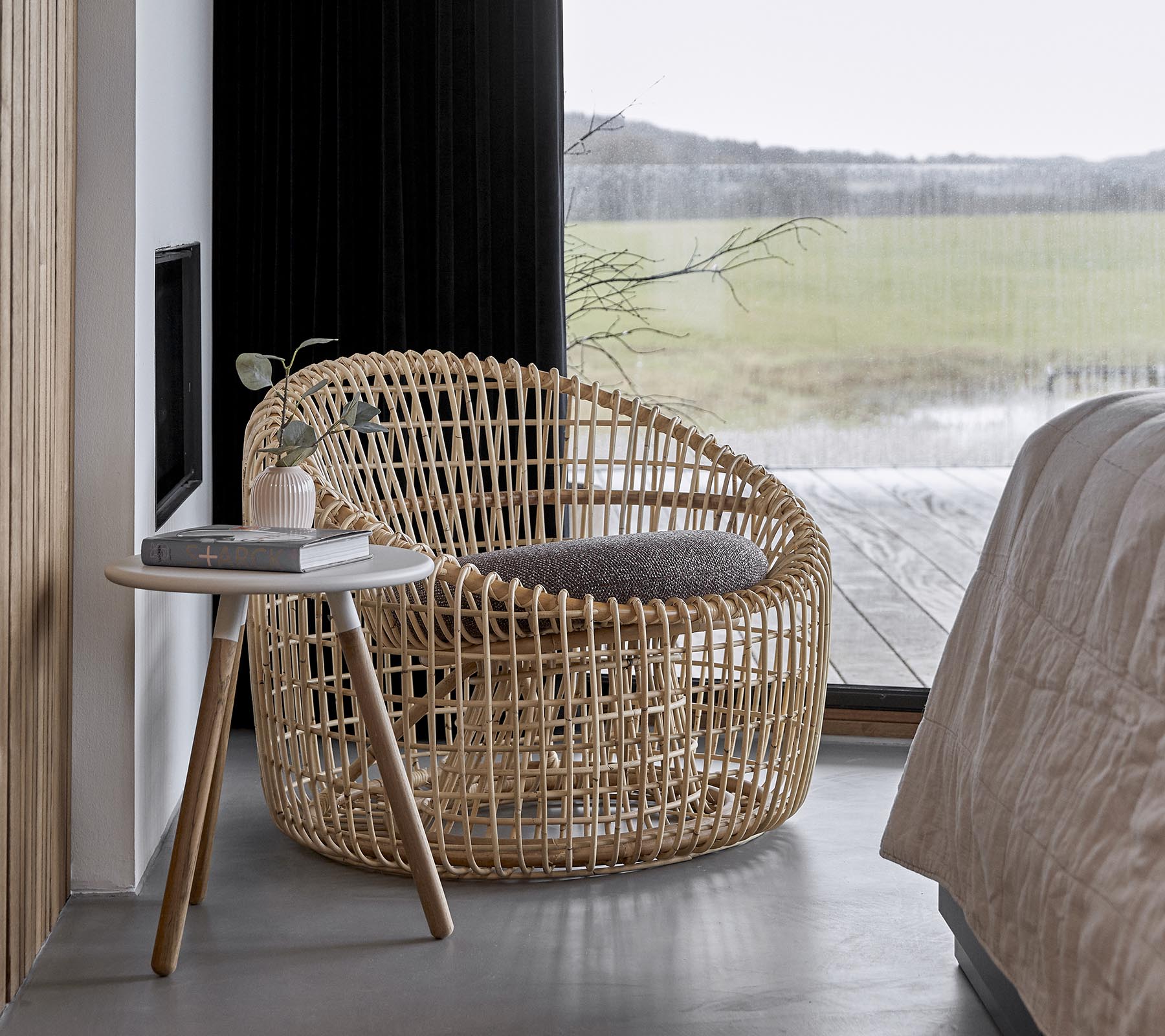 En stilfuld vævet stol parret med et lille sidebord, sat i et roligt miljø med store vinduer, der lader naturligt lys strømme ind.