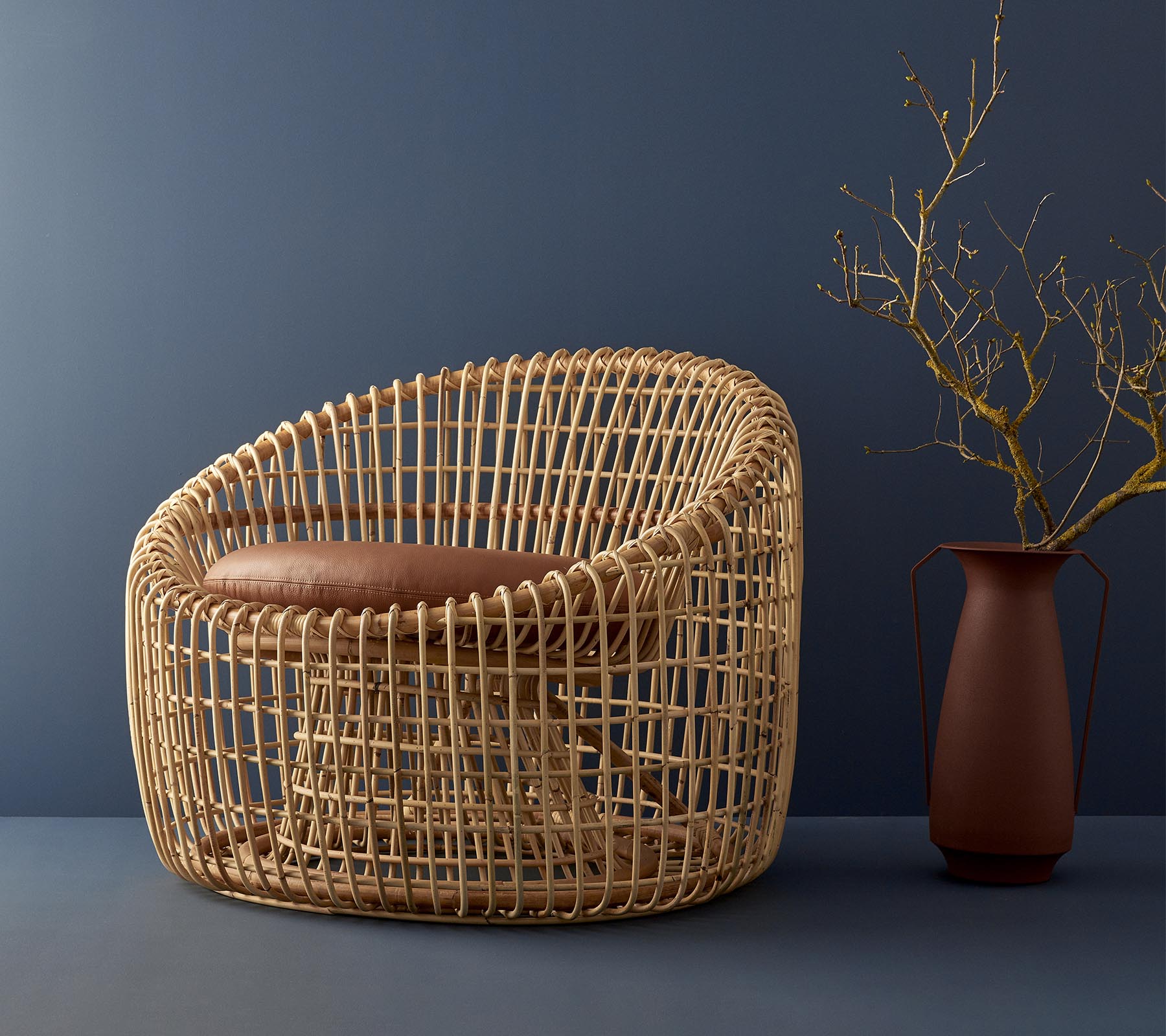 Moderne rokokostol med rundet design, med en polstret sæde og suppleret af en simpel vase med en gren.