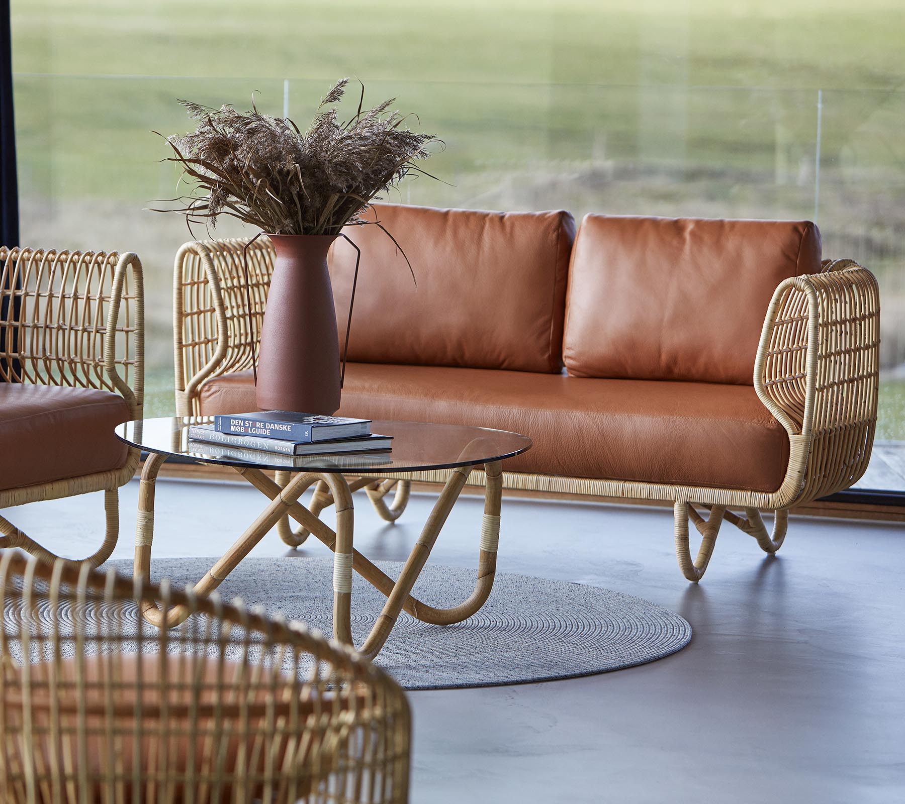 Et stilfuldt siddeområde med en brun lædersofa, et rundt sofabord og dekorative elementer som en vase med tørrede blomster.